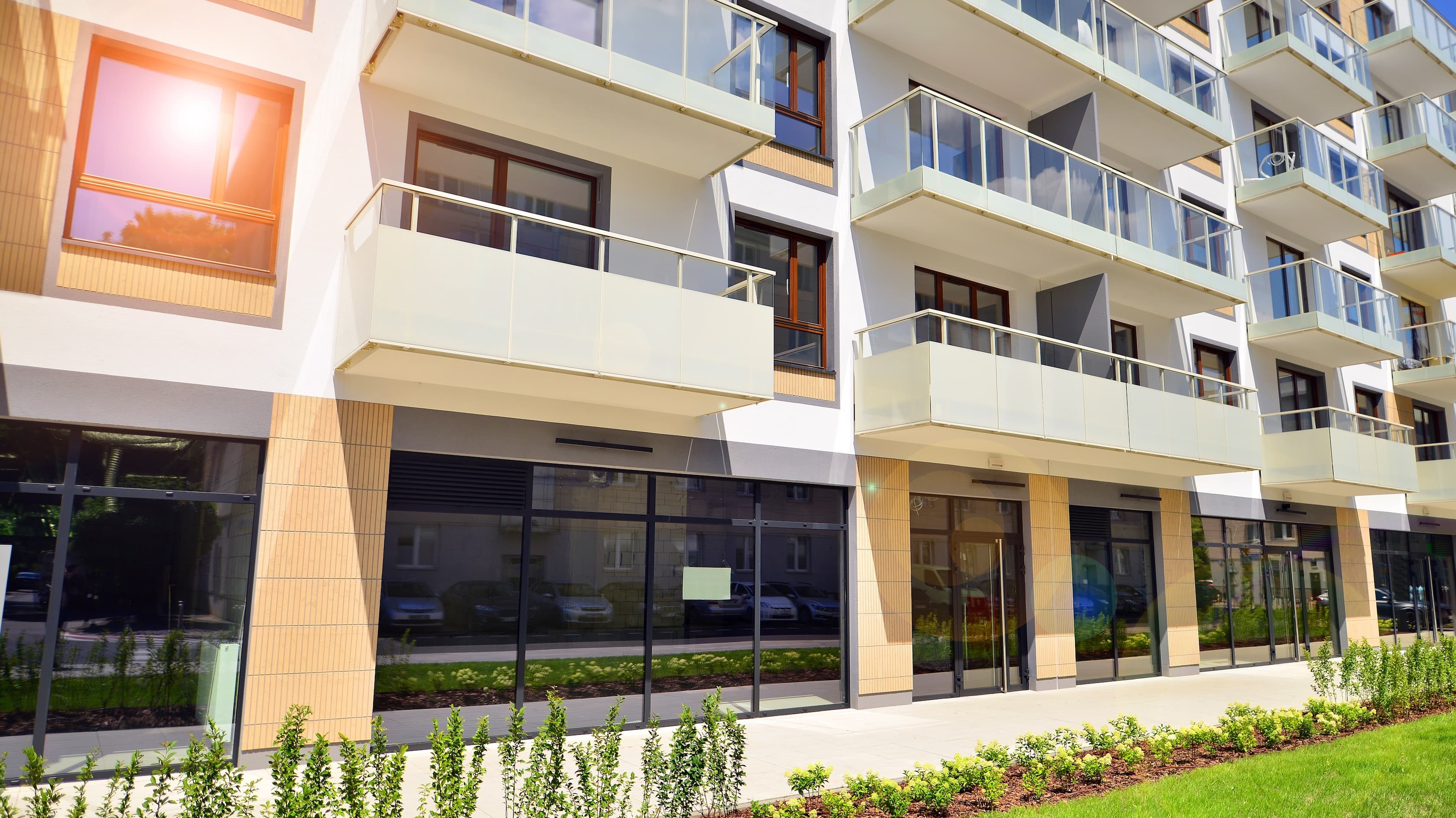 Exterior of modern apartment building with glass balconies in sunlight.