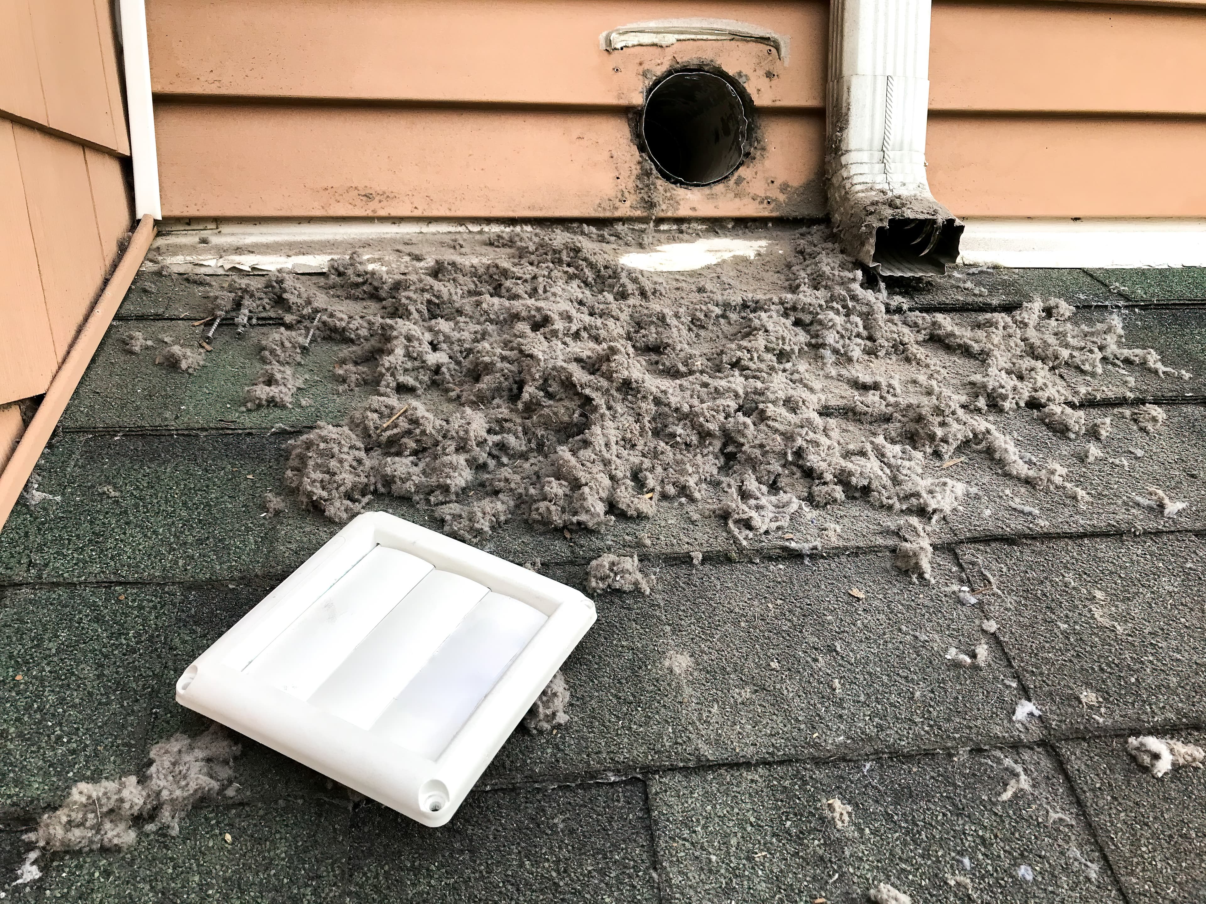 Dryer vent with lint accumulation and detached cover on a roof.