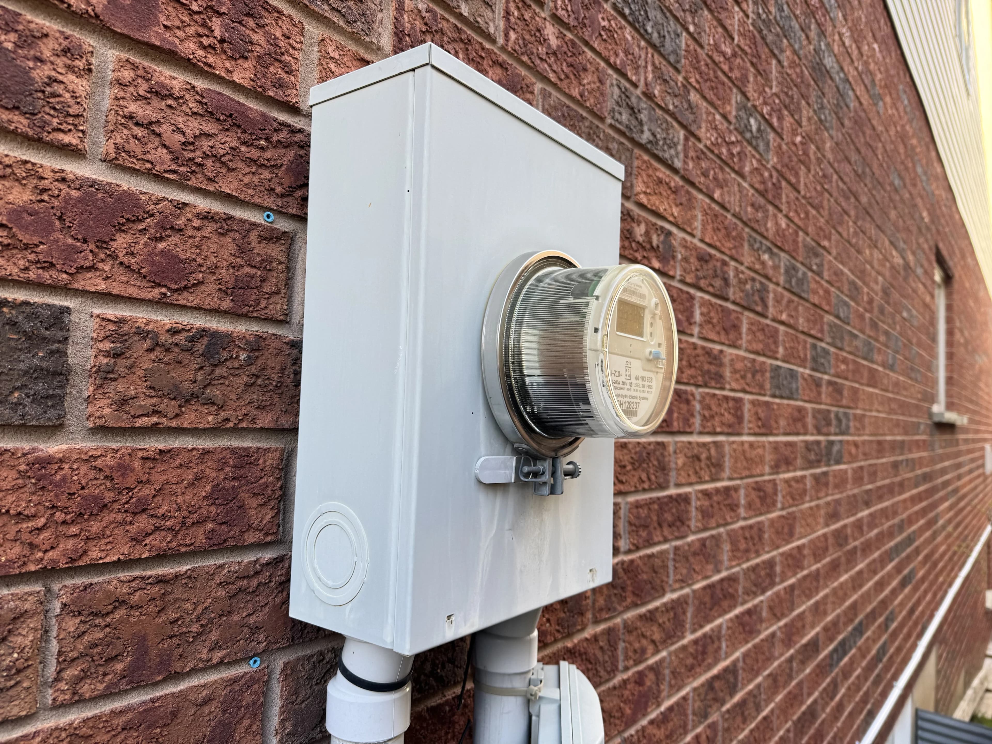 Electric utility meter on a red brick wall in a residential area.