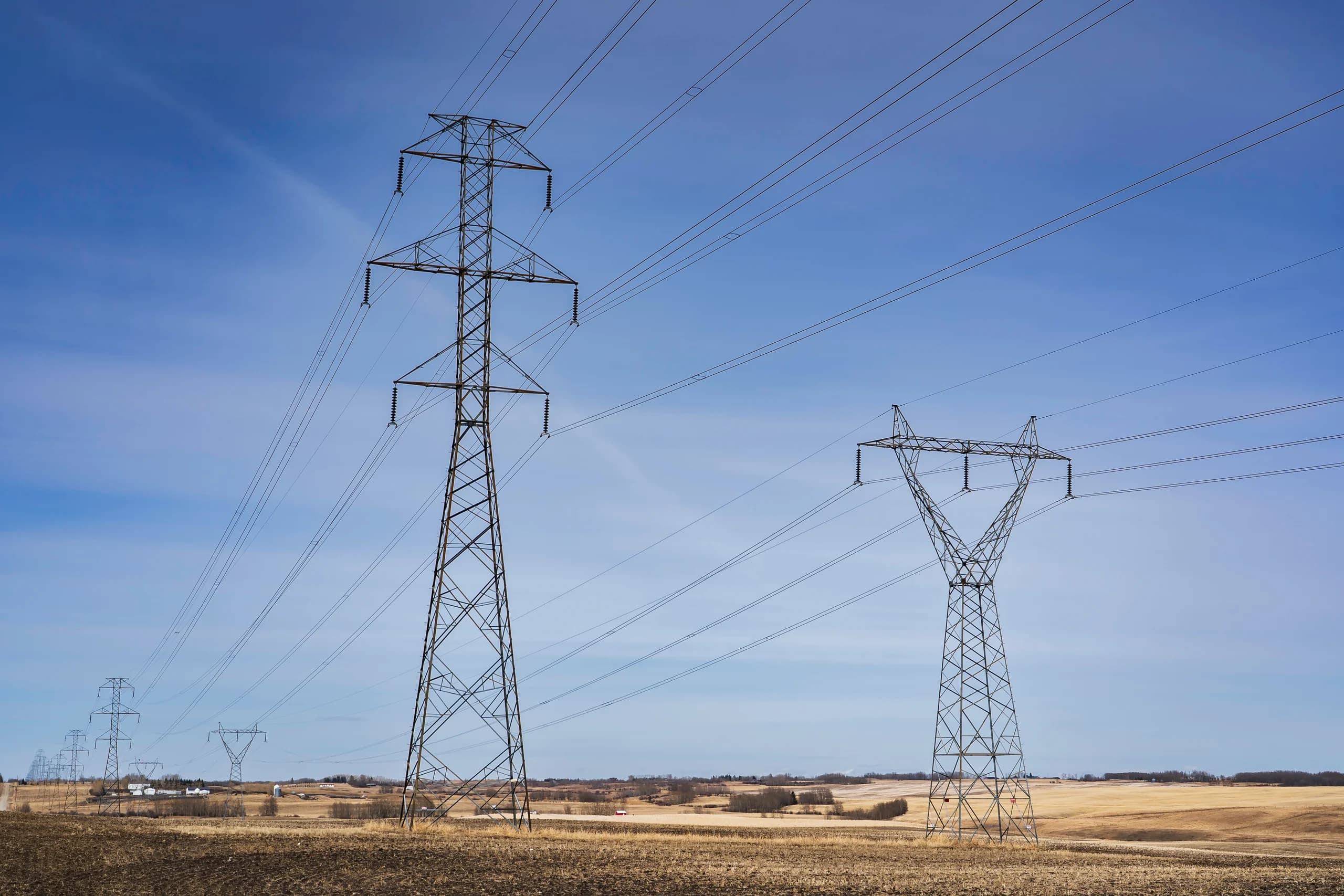 High voltage power lines in an open field under a clear blue sky.