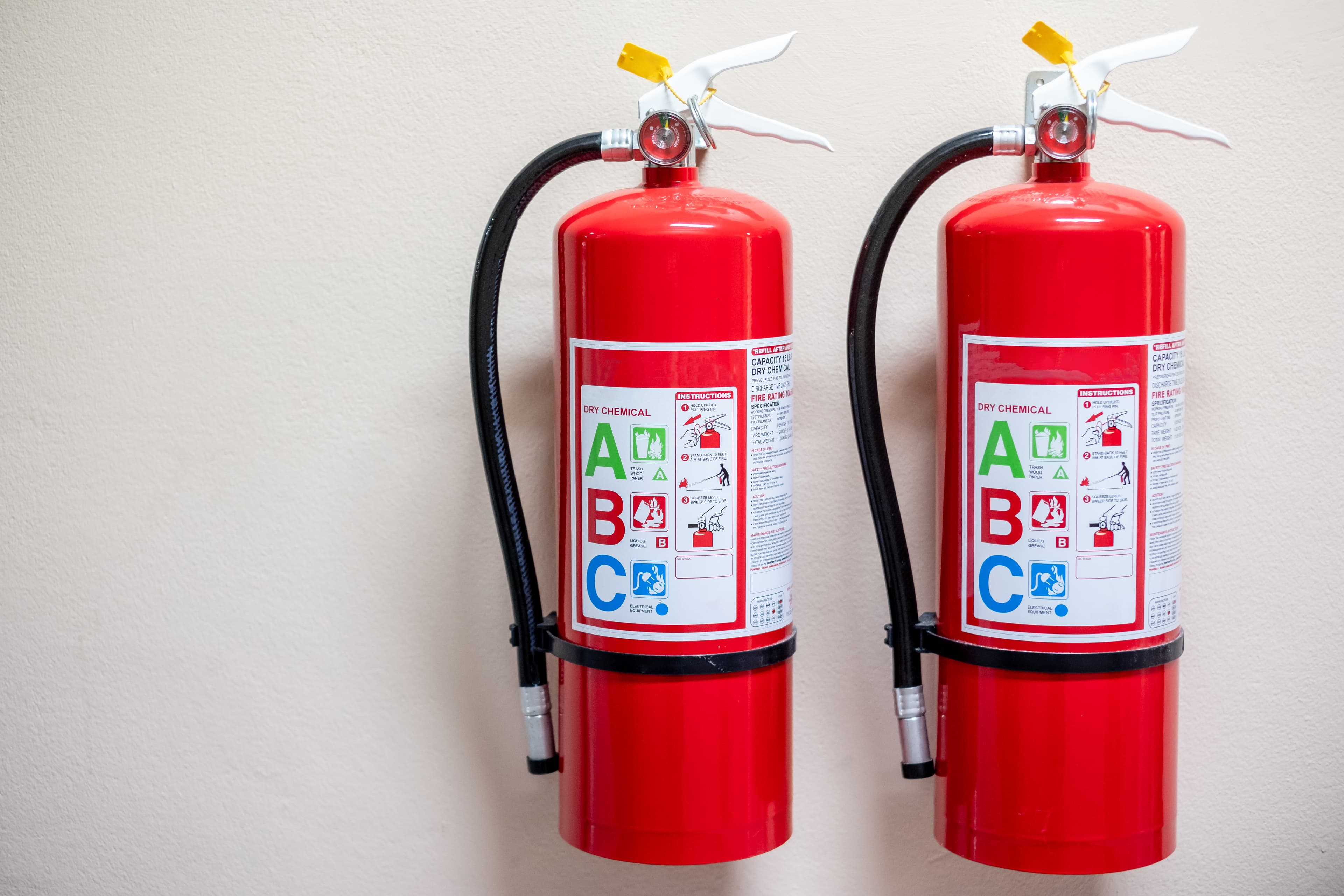 Two red fire extinguishers mounted on a light wall with safety labels.
