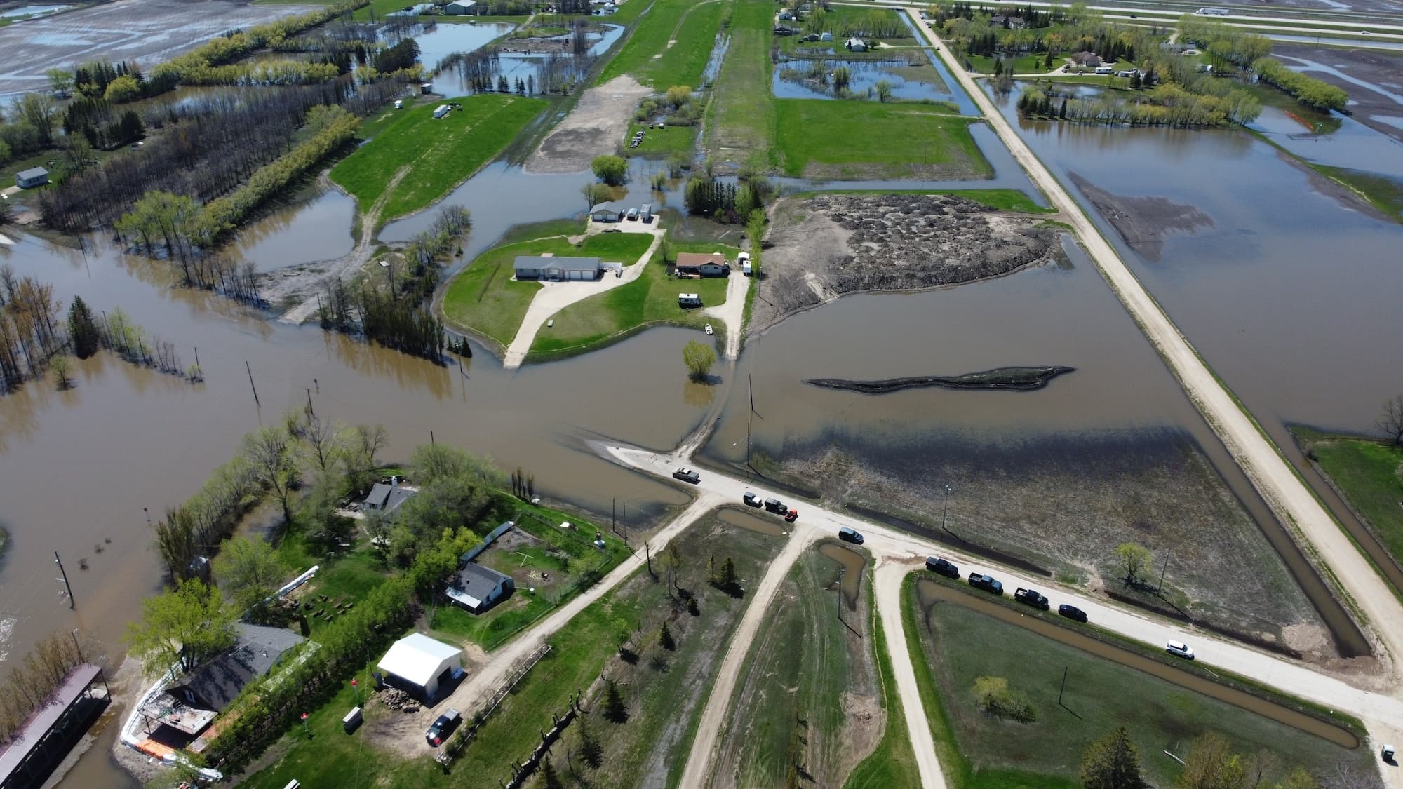 Aerial view of flooded farmland with vehicles on a muddy road.