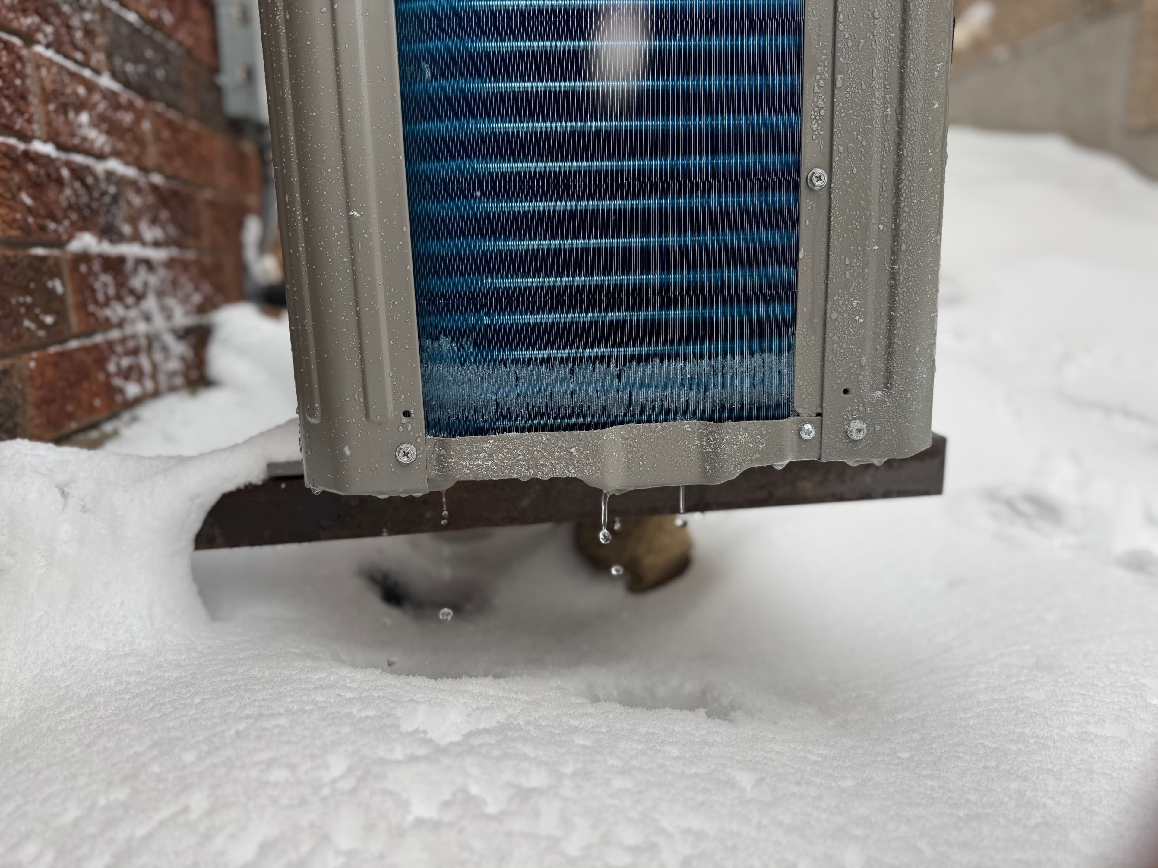 Outdoor heat pump unit with icicles in snowy setting.
