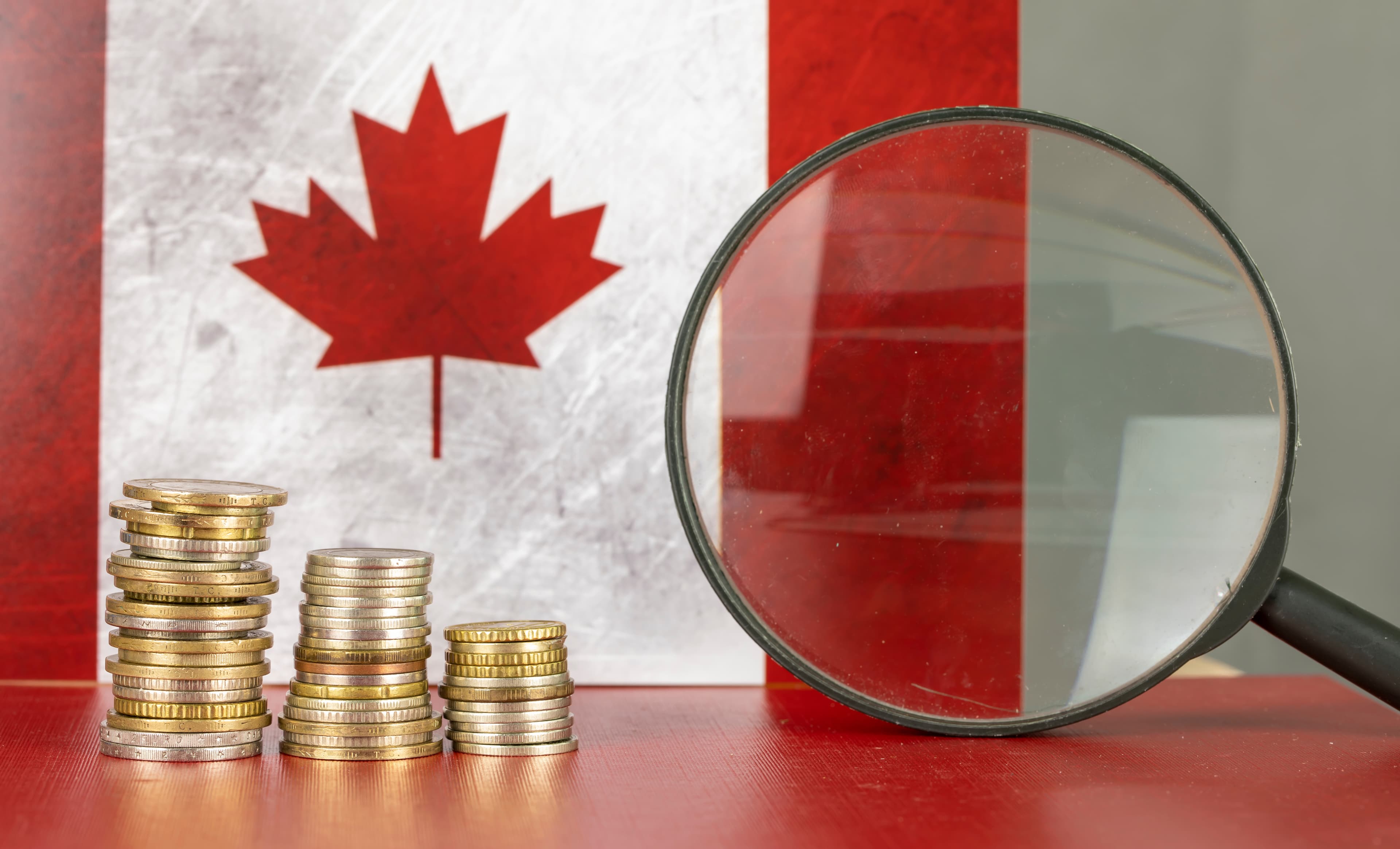 Coins and magnifying glass with Canadian flag background.