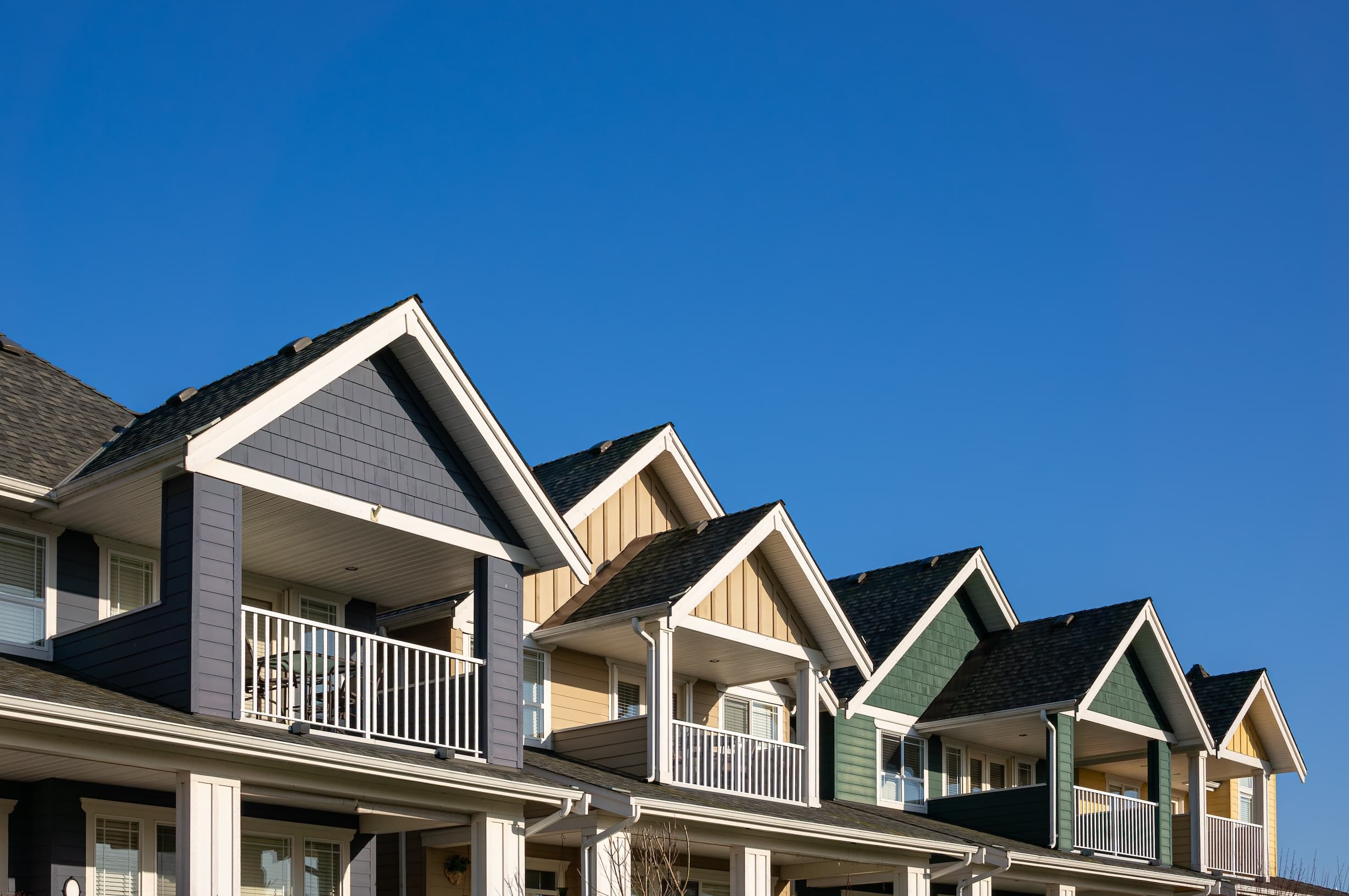 Row of suburban townhouses with varied colors under clear sky.