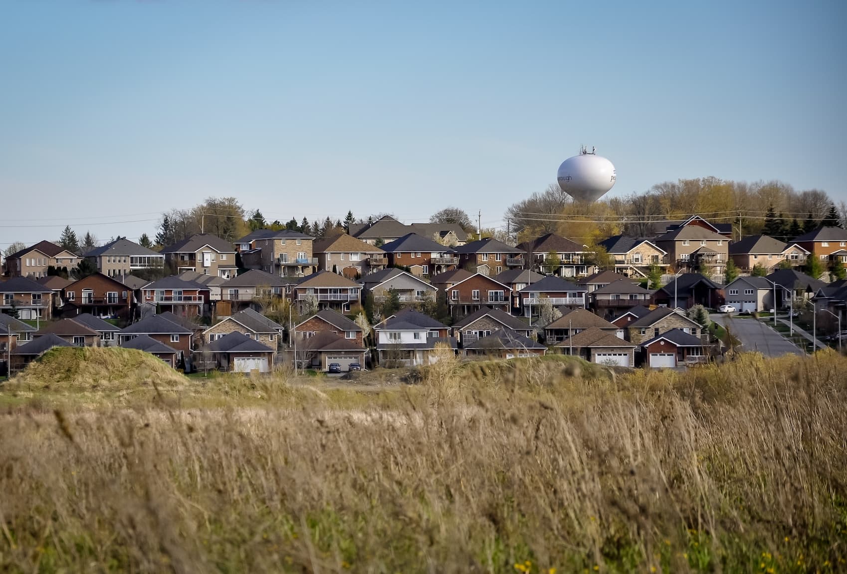 Suburban neighborhood with homes and a water tower under a clear blue sky.