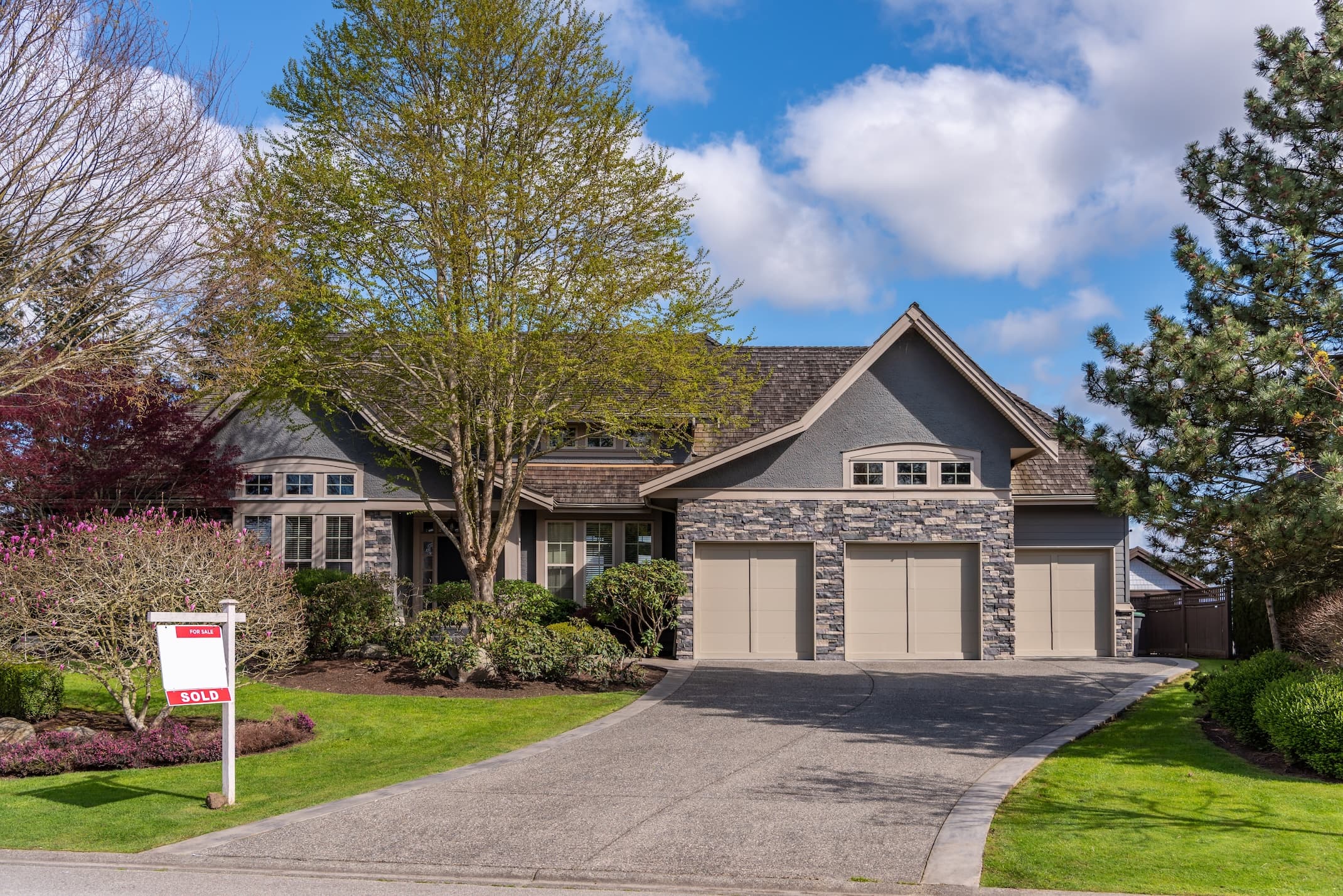 Suburban home with stone facade and sold sign in yard under a blue sky.