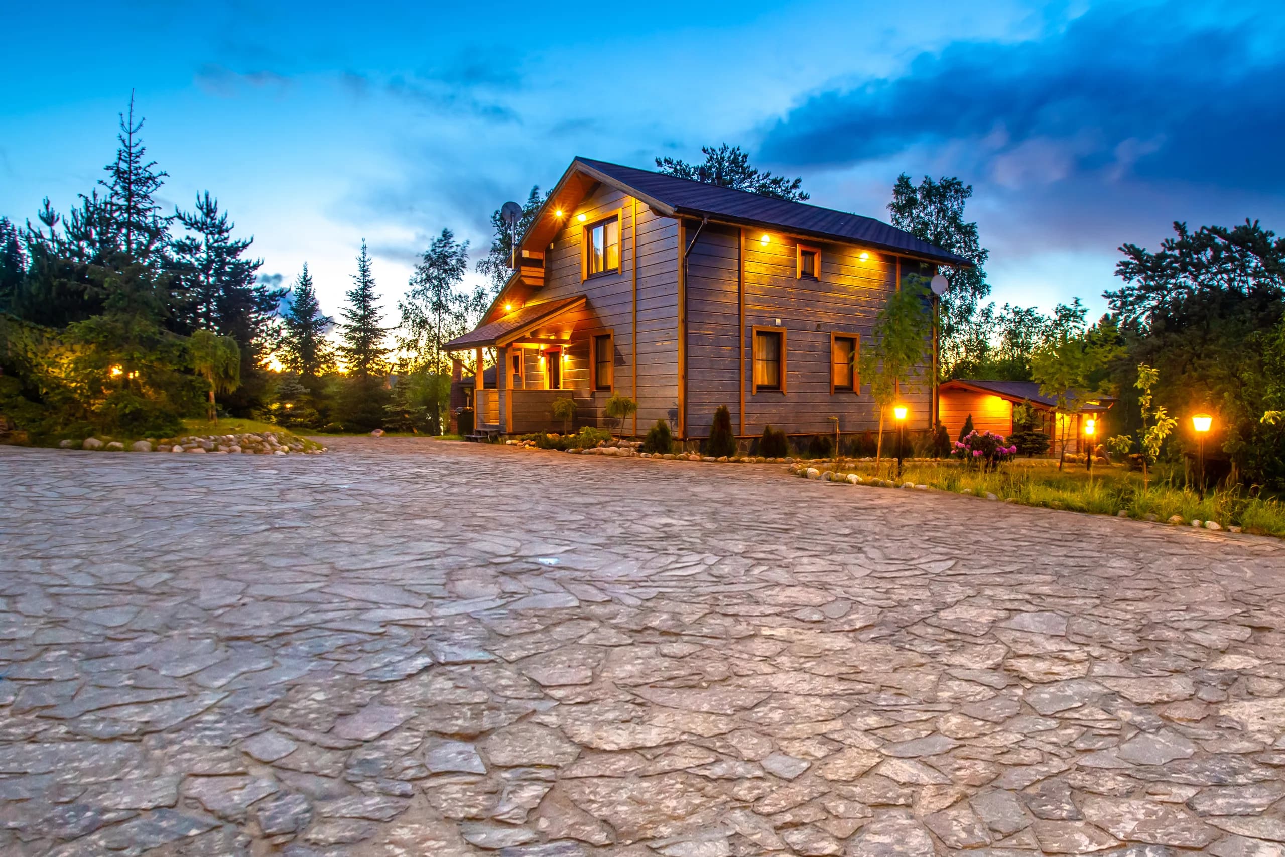 Charming wooden rural home illuminated at dusk with stone pathway.