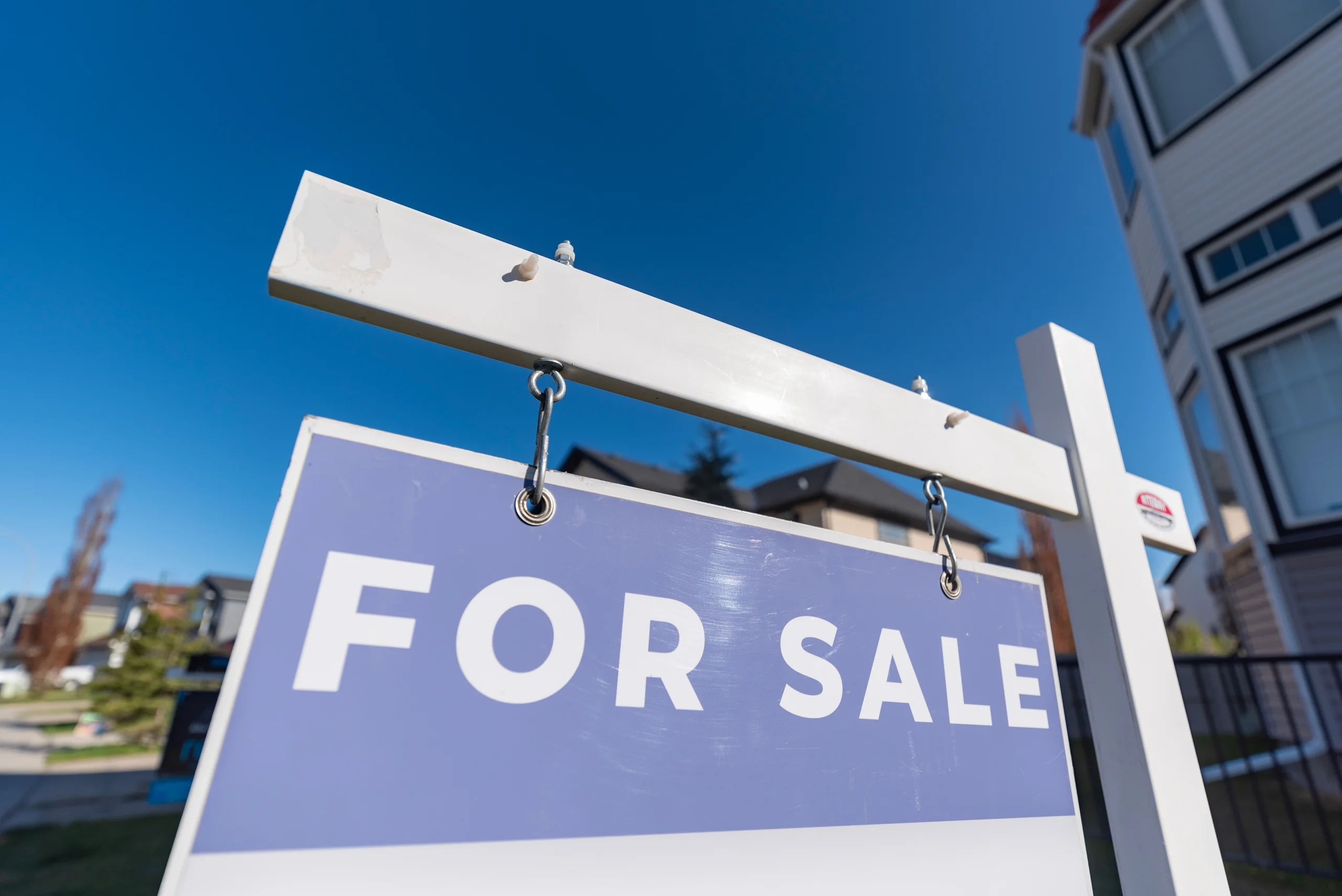For sale sign in front of a house with a blue sky backdrop.