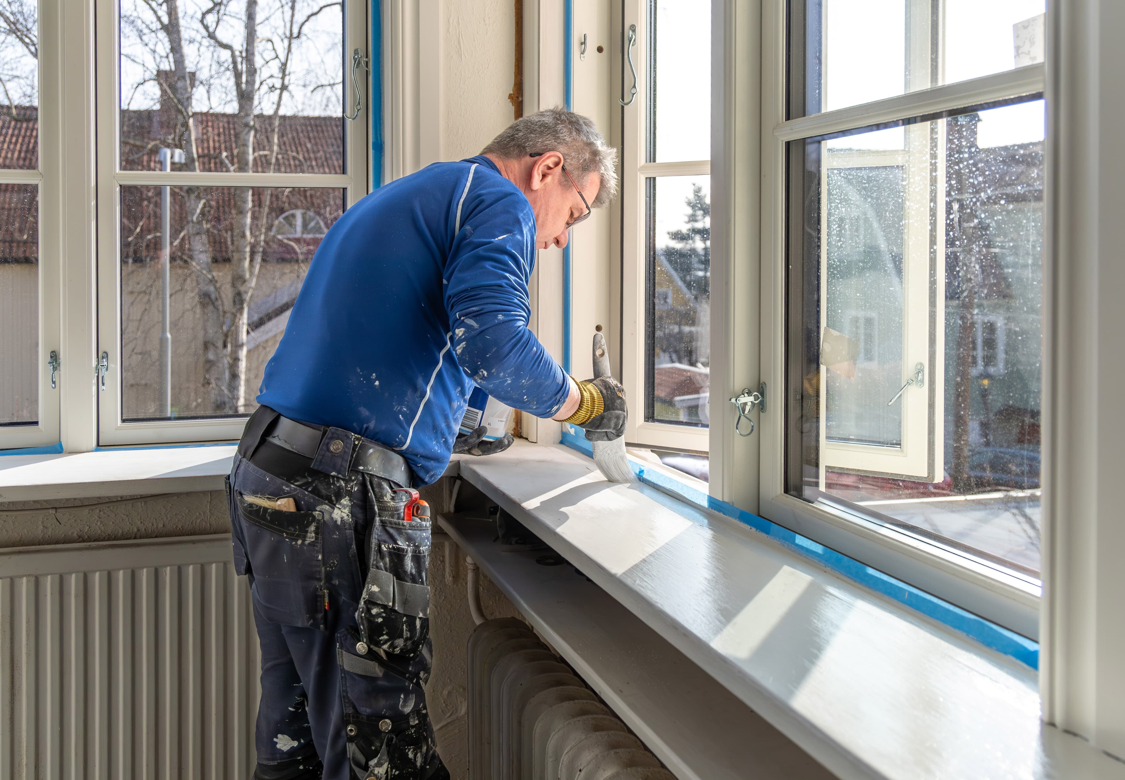 Person painting window sill in sunlit room, renovating home.