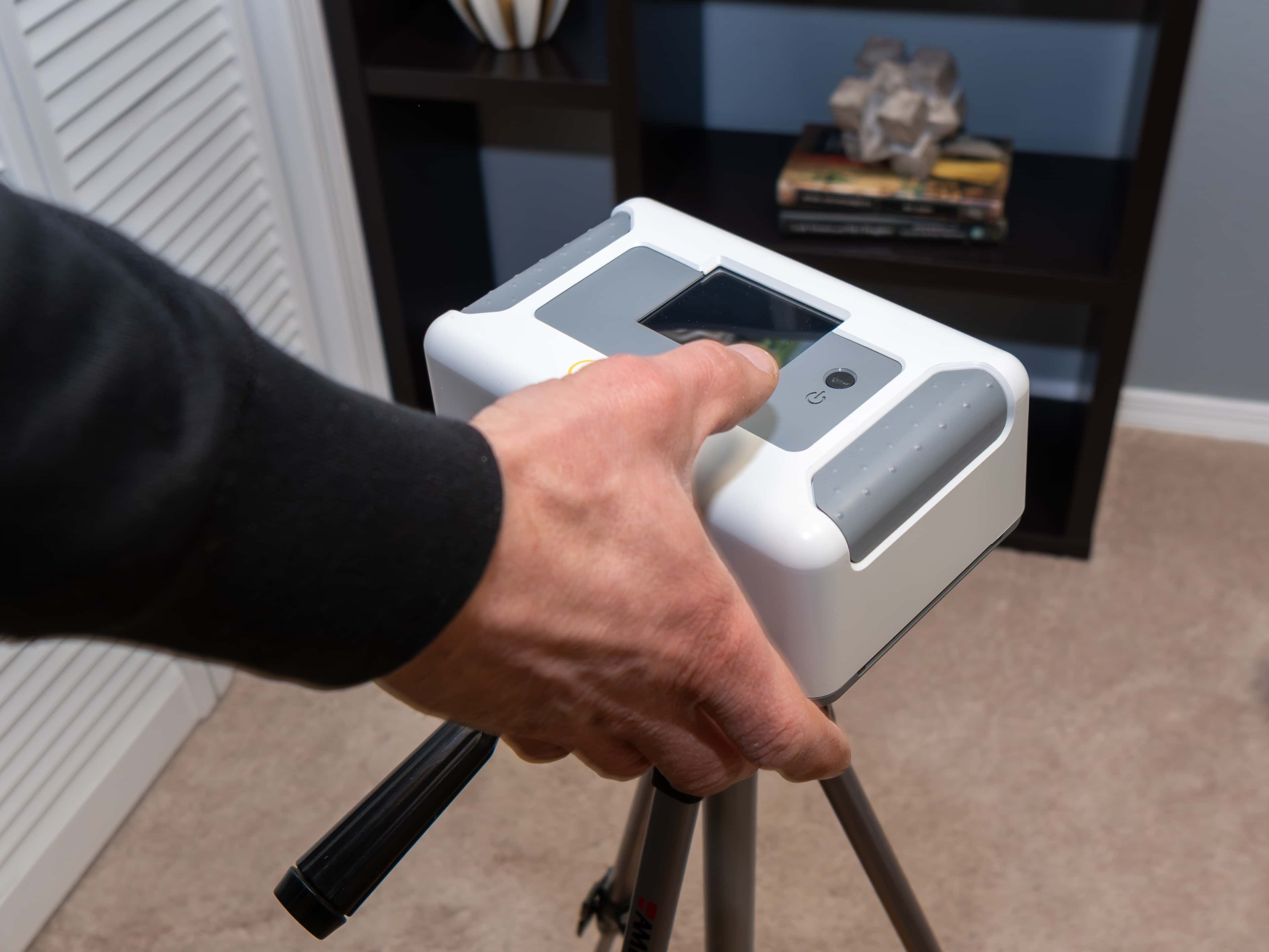Contractor adjusting portable radon detector on tripod in a home.