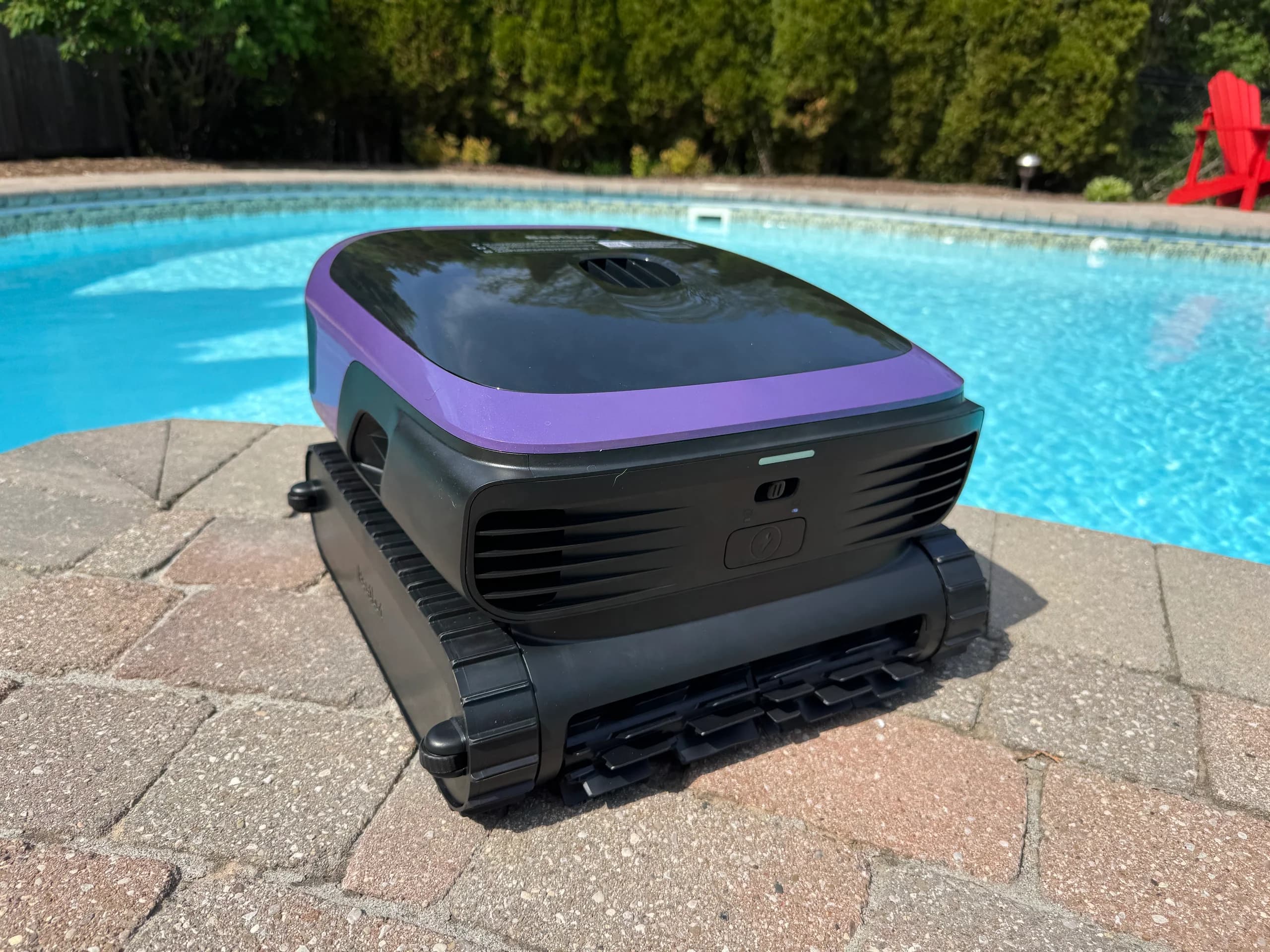 Robotic pool cleaner on poolside tiles, near bright blue water.