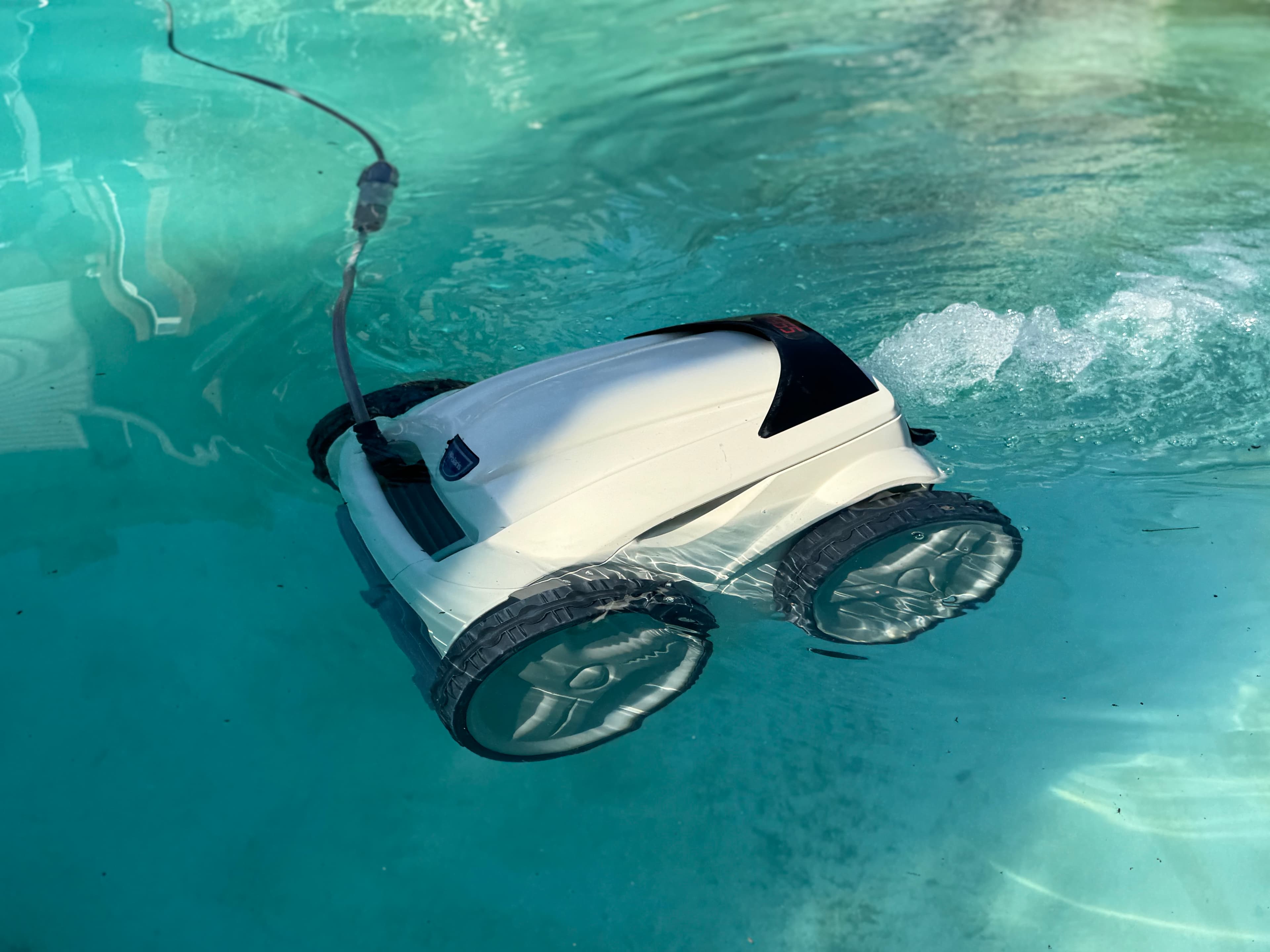 Robotic pool cleaner moving underwater in a bright blue pool.