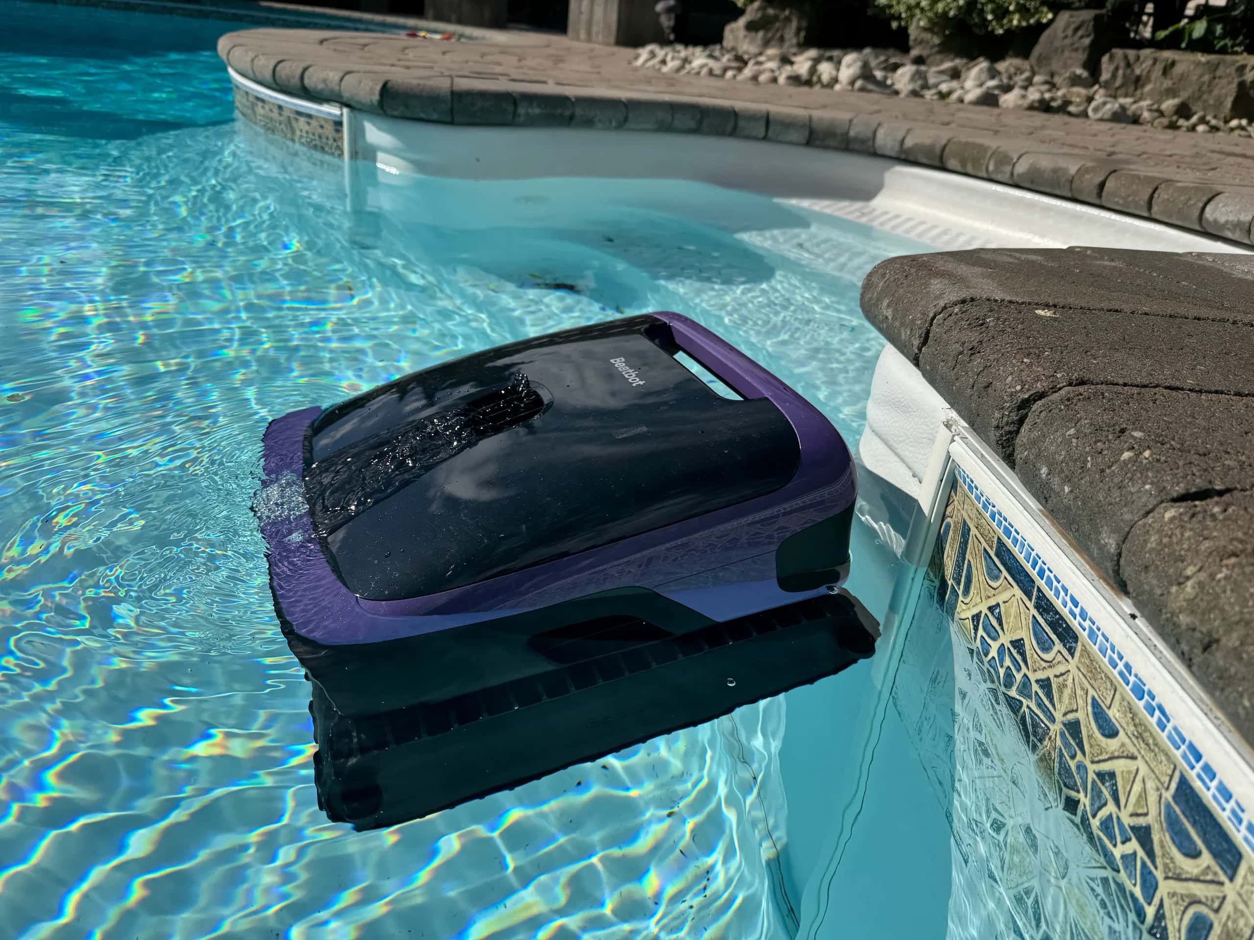 Robotic pool cleaner in swimming pool, under bright sunlight.