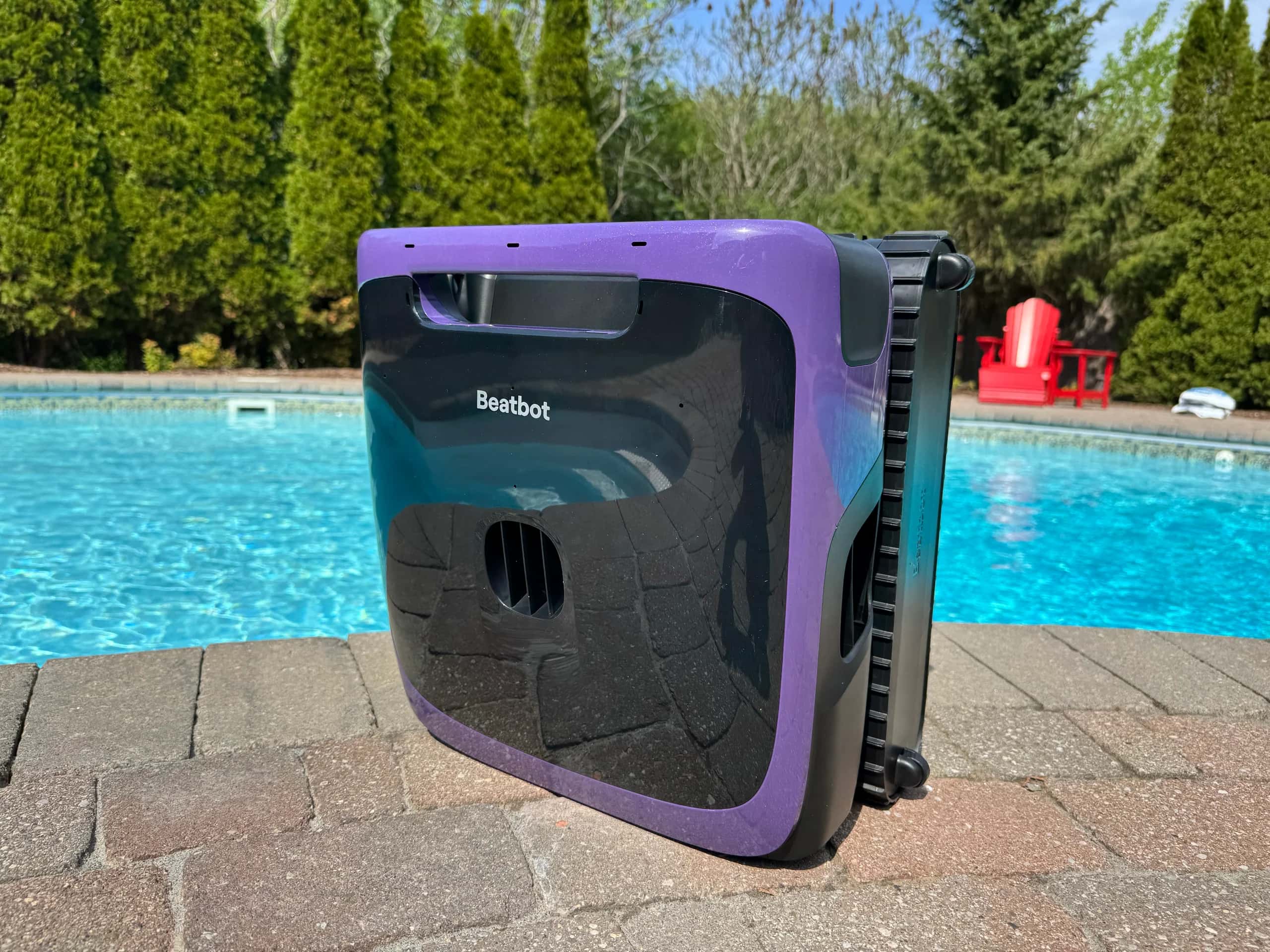 Robotic pool cleaner by Beatbot on pool edge with trees.