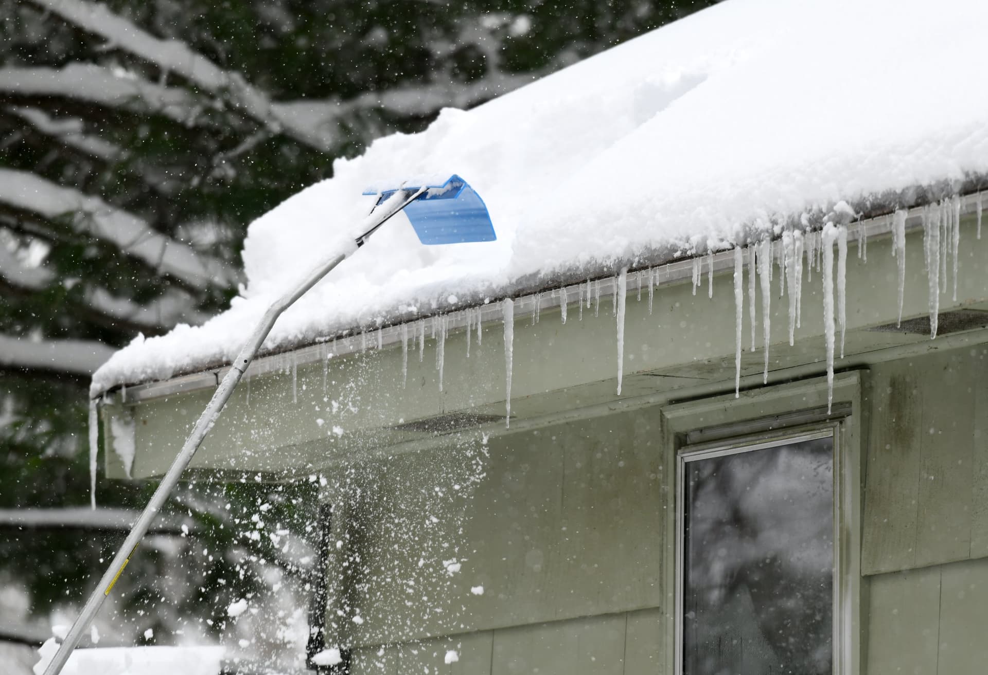 Person using a roof rake to clear snow from a roof.