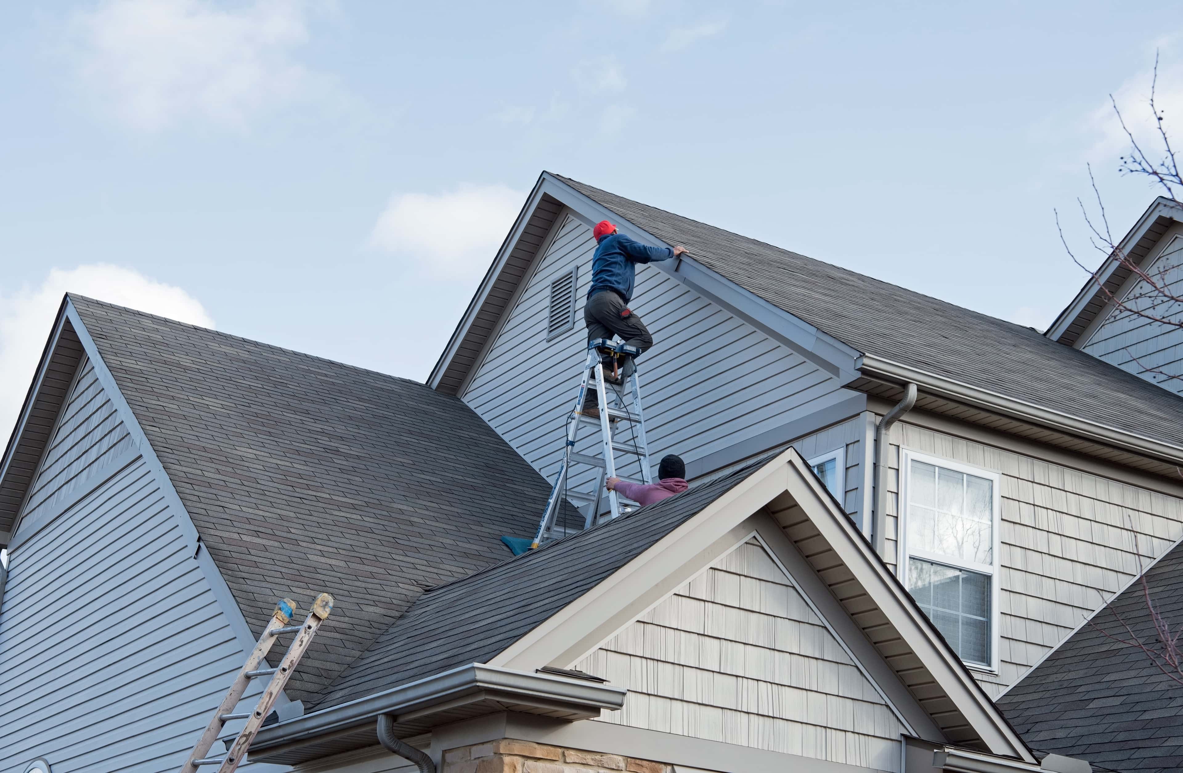 Two workers repairing a roof on a residential home.
