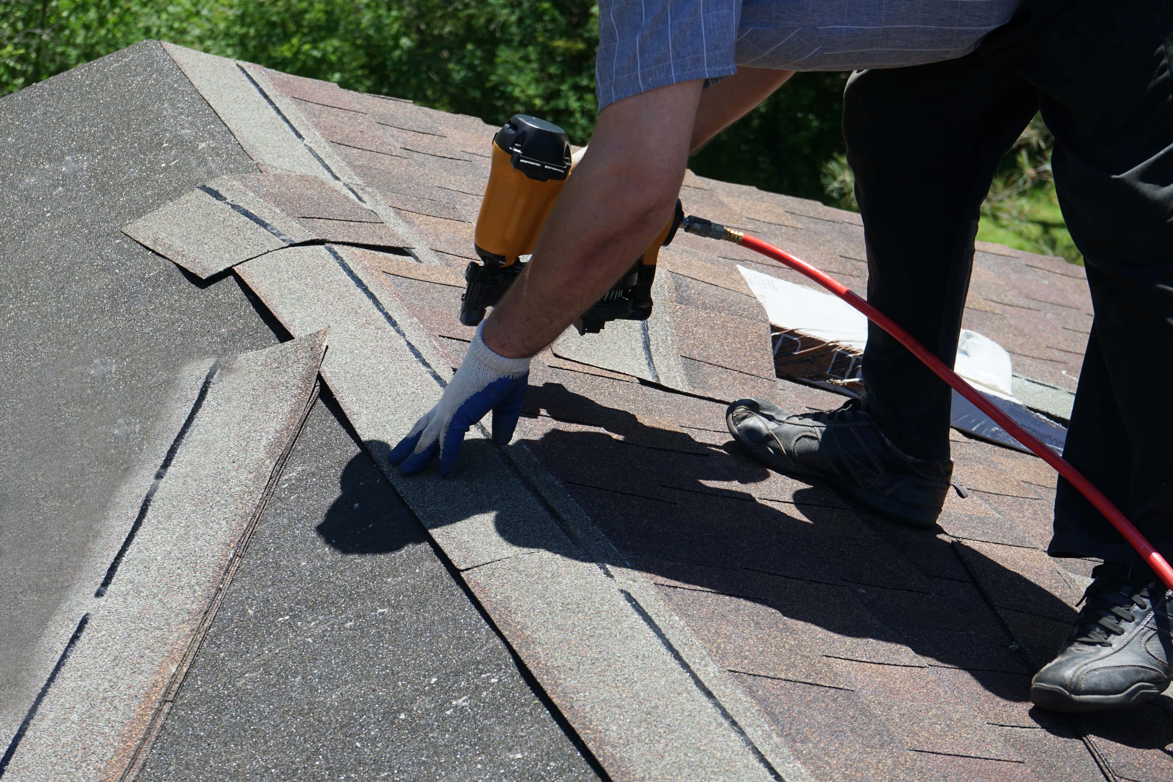 Roofer using a nail gun to install shingles on a rooftop.