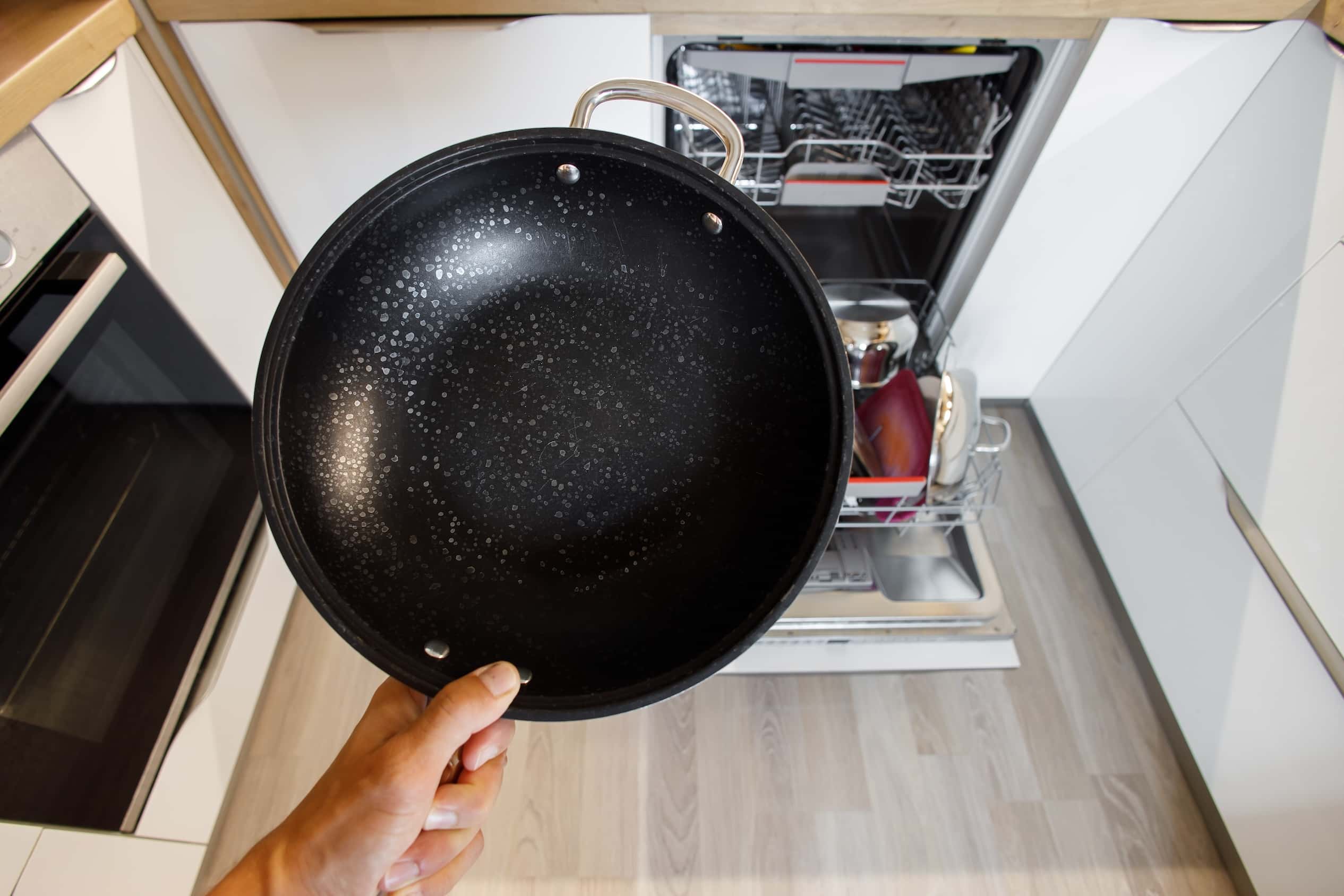 Person holding a black pan over an open dishwasher.