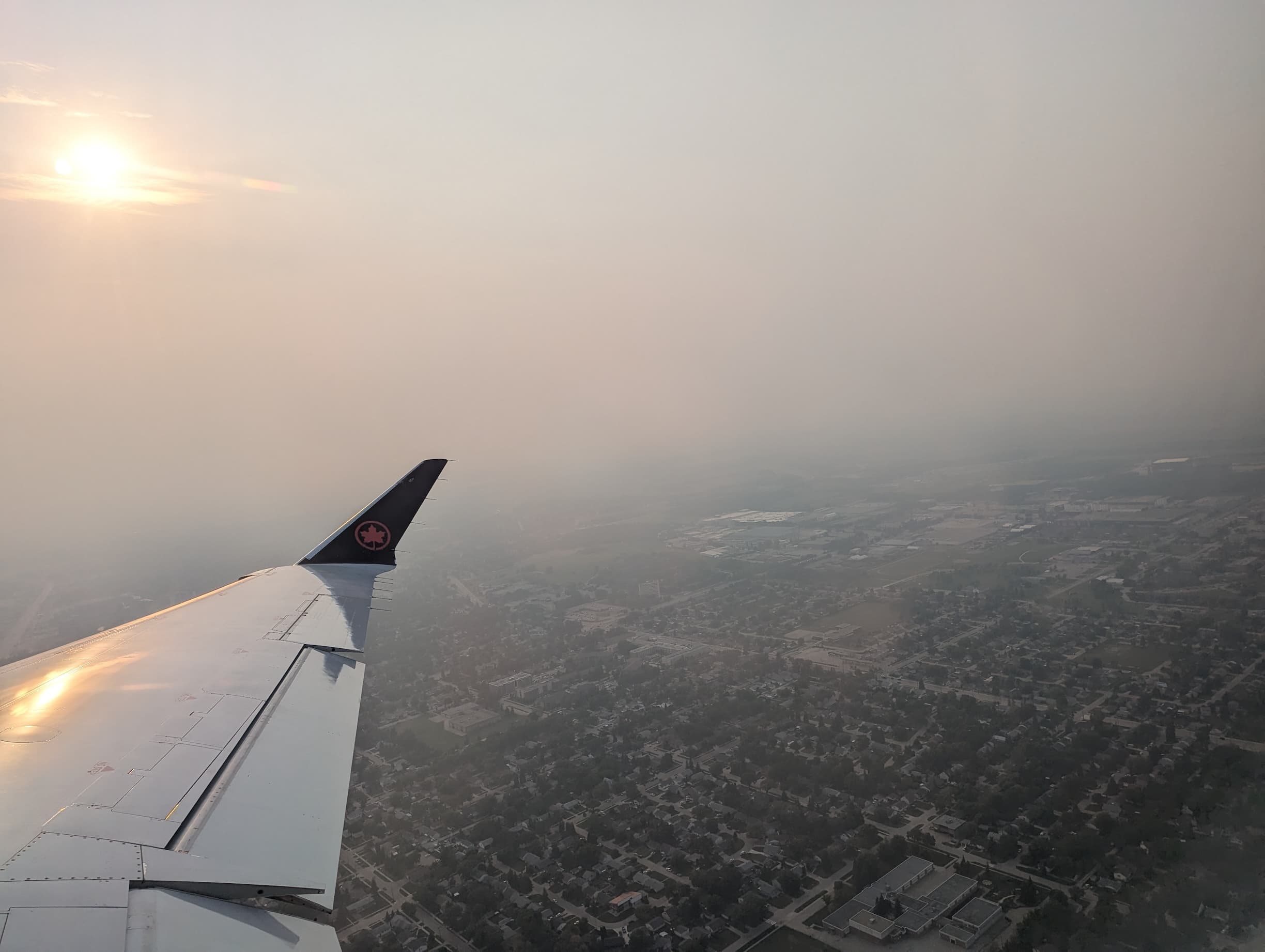 Aerial cityscape covered in smoke with visible airplane wing.